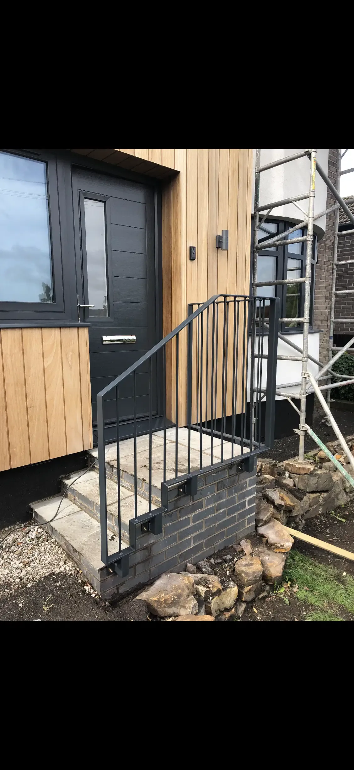 Dark steel railing fitted beside new front entrance steps on a house with timber cladding