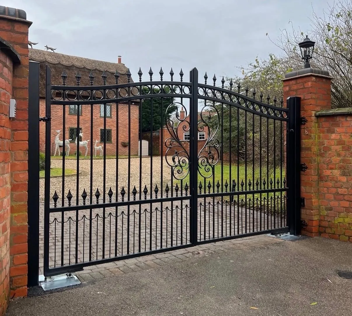 Black ornamental steel driveway gate fitted between brick gateposts outside a house